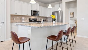 Eine moderne Küche mit weißen Schränken, einer Granit Arbeitsplatte, Edelstahlgeräten und drei Barhocker.