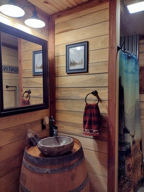 Une salle de bain rustique avec des murs en bois, un lavabo en forme de tonneau en bois, un miroir et des tableaux encadrés.