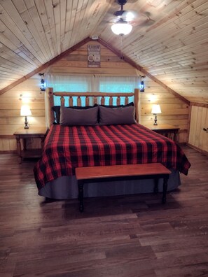 Une chambre de style cabane avec un plafond en bois, un lit recouvert d’une couverture à carreaux rouges et noirs, deux lampes de chevet et un banc en bois.