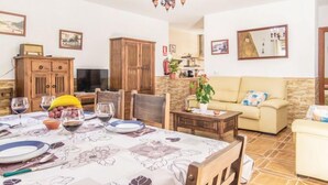 Zona pranzo con tavolo apparecchiato per quattro persone, un divano e una televisione sullo sfondo.