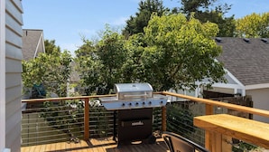 Un patio con una parrilla, terraza de madera y vistas a casas y árboles vecinos.