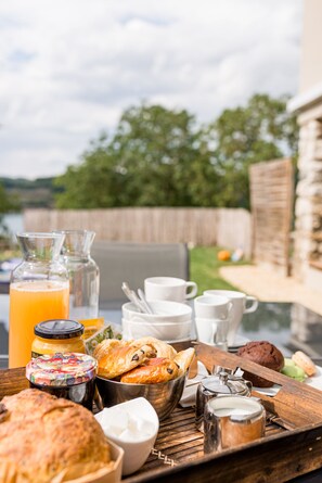 A breakfast tray with pastries, coffee, and juice on an outdoor table with a view of a wooden fence and greenery. - Maison Avec vue sur le Lac, Plage 200m (Bilieu)