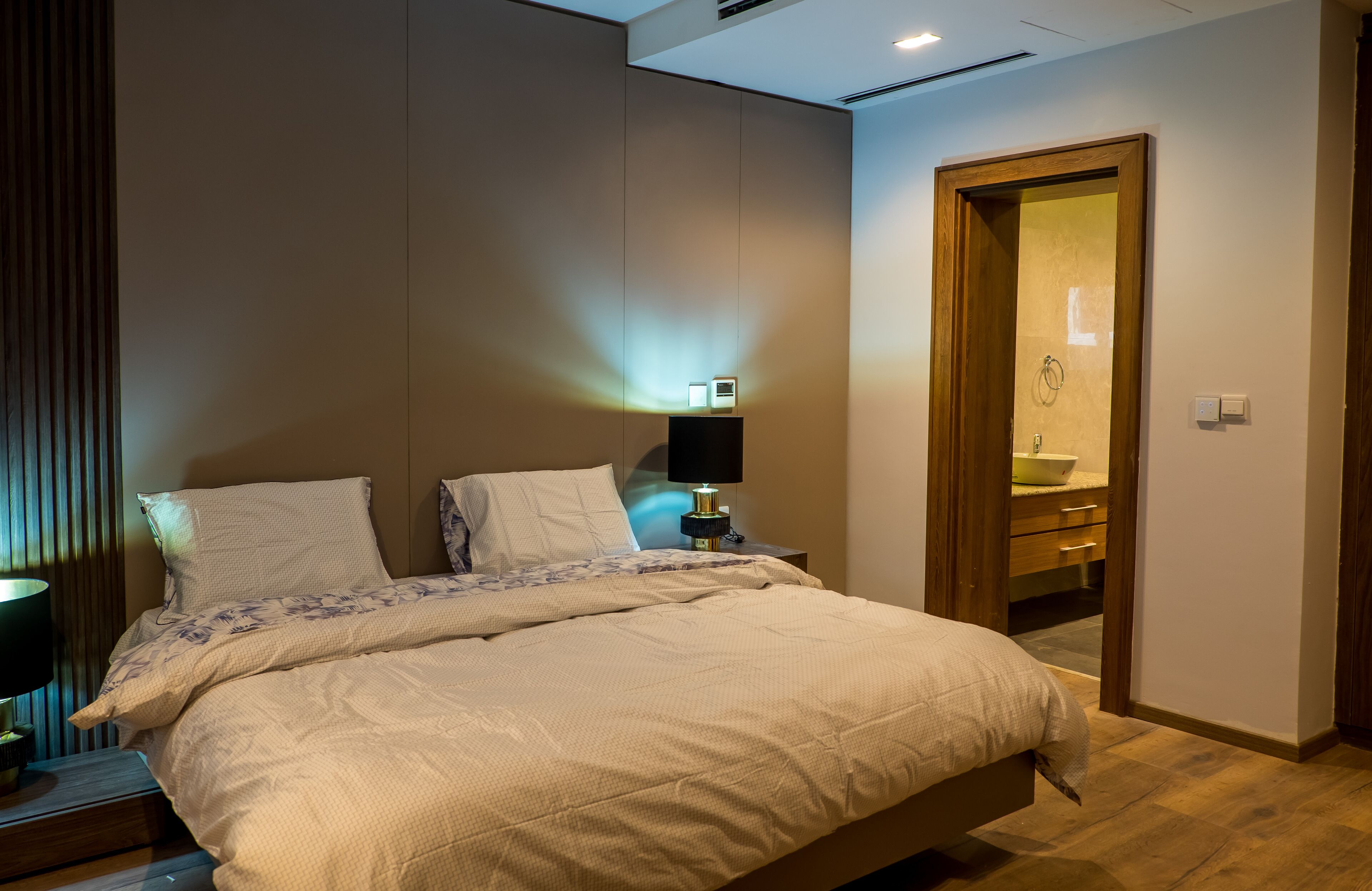 A modern bedroom with a large bed, bedside tables, a nightstand, and a bathroom visible through an open door.
