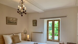 Una camera da letto con un letto grande, un lampadario, una finestra vista verde e un termosifone.
