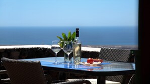 Ein Tisch mit einer Flasche, Gläsern und einer Tomate auf einer blauen Matte mit Blick auf den Ozean.