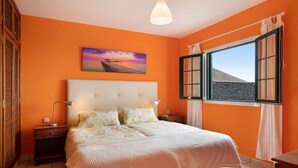 Ein Schlafzimmer mit Bett, Nachttischen, einem Gemälde, einem Fenster mit Vorhängen und Blick auf ein Gebäude.