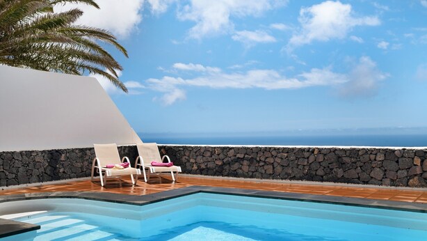 Ein Pool mit zwei Liegestühlen, einer Steinmauer und Blick aufs Meer.
