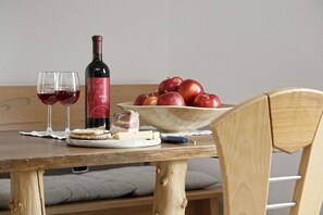 Una mesa de madera con una botella de vino, copas, manzanas, queso y galletas.