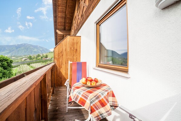 Un balcón con baranda de madera, una mesa con mantel a cuadros y un frutero con fruta.