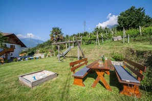 Un banco de madera y una mesa de picnic en un área con césped y vistas a la montaña.