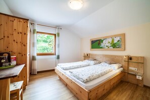 A bedroom with two beds, a wooden desk, a window with curtains, and a painting on the wall.