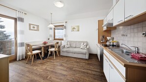 A compact kitchen with a dining area, wooden flooring, and a view through a window. - Apartment "Langeshof - Abendrot" with Mountain View, Wi-Fi, Balcony & Garden (Kuens bei Meran, Südtirol - Italien)