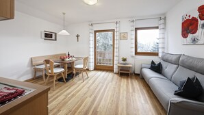 A modern living room with a grey sofa, wooden dining table, and chairs. - Apartment "Langeshof - Abendrot" with Mountain View, Wi-Fi, Balcony & Garden (Kuens bei Meran, Südtirol - Italien)