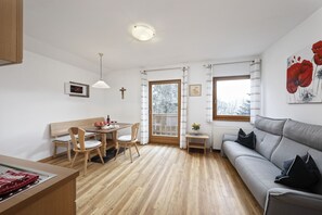 A modern living room with a grey sofa, wooden dining table, and chairs. - Apartment "Langeshof - Abendrot" with Mountain View, Wi-Fi, Balcony & Garden (Kuens bei Meran, Südtirol - Italien)