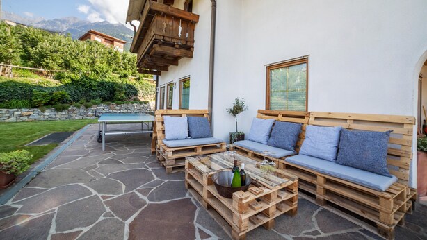 An outdoor seating area with wooden benches and a table, stone flooring, and a view of mountains. - Apartment "Langeshof - Abendrot" with Mountain View, Wi-Fi, Balcony & Garden (Kuens bei Meran, Südtirol - Italien)