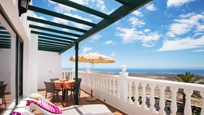 A balcony with white chairs, a table, and an umbrella, overlooking a coastal view. - Vacation Apartment “La Vega de Lanzarote 4” with Sea View, Pool & Wi-Fi (Tías)