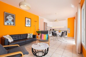 A modern living room with a black sofa, a round coffee table, and a dining area with a white table and chairs.