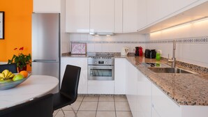A modern kitchen with white cabinets, a stainless steel refrigerator, a built-in oven, and a granite countertop. - Vacation Apartment “La Vega de Lanzarote 4” with Sea View, Pool & Wi-Fi (Tías)
