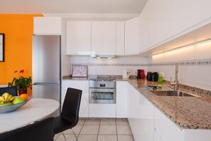 A modern kitchen with white cabinets, a stainless steel refrigerator, a built-in oven, and a granite countertop.