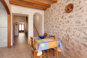 Un coin repas avec une table dressée pour quatre personnes, un mur en pierre et un escalier menant à une autre pièce.