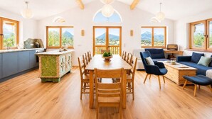 Amplia sala de estar con mesa de comedor de madera, sofá azul y ventanas grandes que ofrecen vistas a la montaña.
