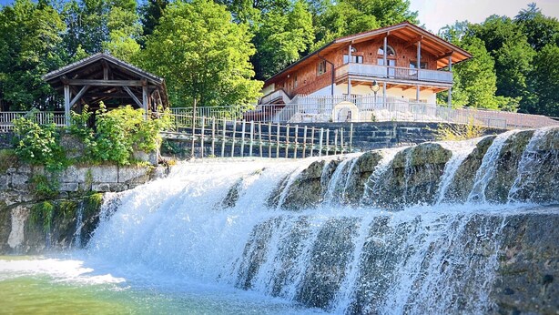 Una cabaña de madera con balcón, una pequeña construcción de madera y una cascada.