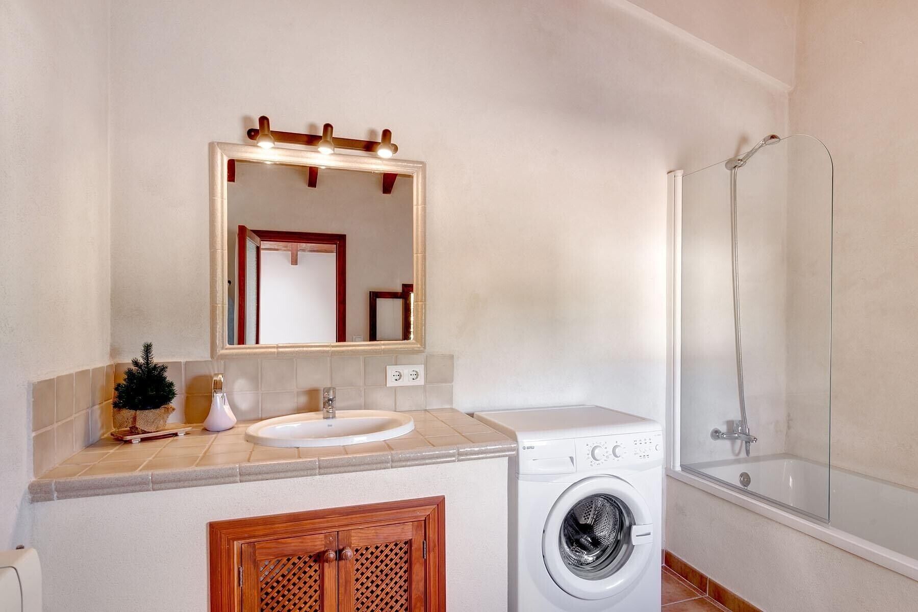 A bathroom with a sink, mirror, washing machine, and shower.