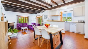 Une cuisine moderne avec des meubles blancs, une table à manger en bois et un canapé violet.