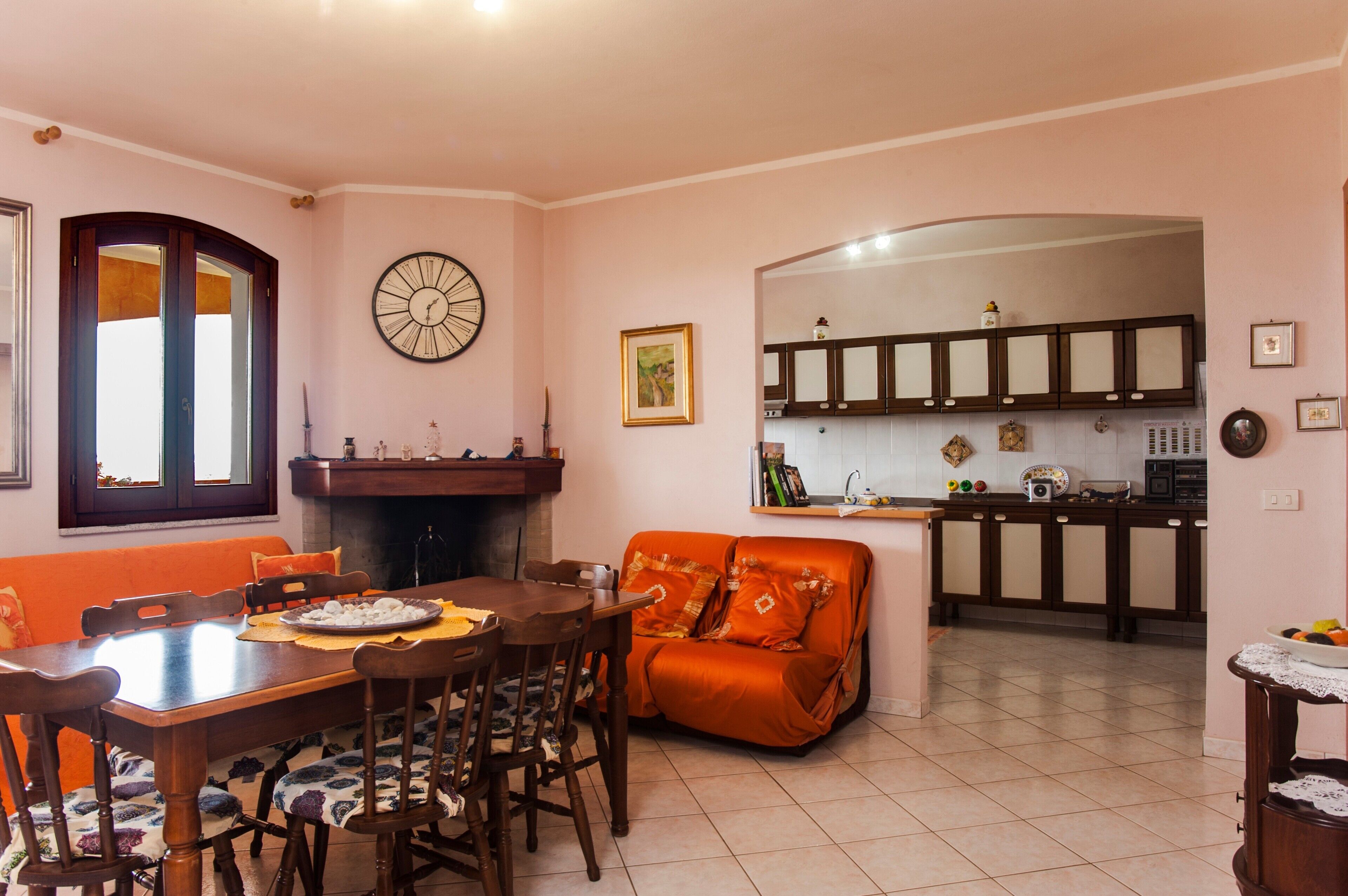 Un coin repas avec une table en bois, des chaises et un canapé orange. Une horloge et un tableau encadré sont accrochés au mur.