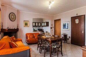 Un salon comprenant un canapé, une table à manger, des chaises, une cheminée, des meubles de cuisine et une horloge murale.