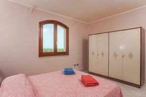 Une chambre à coucher avec un lit, une armoire, une fenêtre donnant sur un beau paysage et une porte.