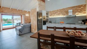 A modern kitchen with a built-in oven, a dining area with a wooden table and chairs, and a large sliding glass door leading to a pool. - Holiday Home Can Tianet with Mountain View, Pool, Wi-Fi & Terrace (Randa)