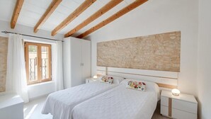 A bedroom with two beds, a stone wall, wooden beams, a window with curtains, and bedside lamps. - Holiday Home Can Tianet with Mountain View, Pool, Wi-Fi & Terrace (Randa)