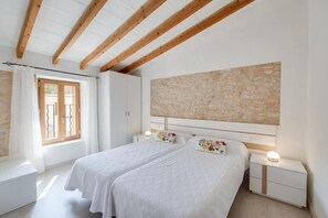 Ein Schlafzimmer mit zwei Betten, einer Steinwand, Holzbalken, einem Fenster mit Vorhängen und Nachttischlampen.