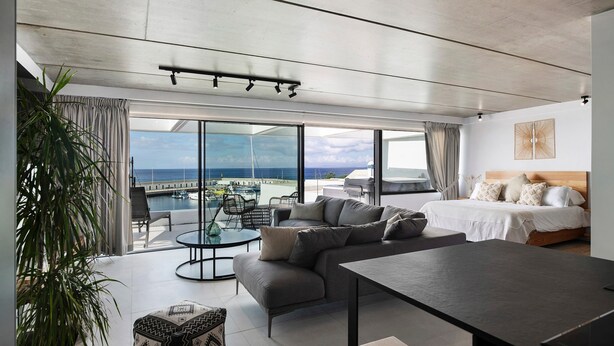 Een moderne hotelkamer met een groot bed, een bank, een eettafel en een balkon met uitzicht op zee.