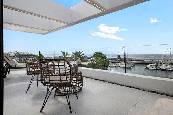 A terrace with wicker chairs, a view of the marina, and a clear sky.