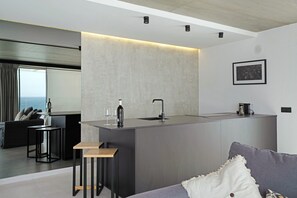 Eine moderne Küche mit Kochinsel, ein Essbereich mit Sofa und Tisch sowie Meerblick durch ein großes Fenster.