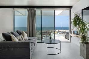 Ein modernes Wohnzimmer mit einer Couch, einem runden Tisch und Meerblick durch große Glasfenster.
