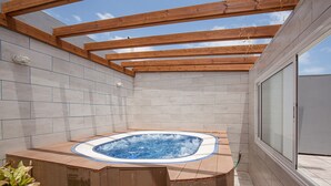 A hot tub in a covered outdoor area with wooden beams and tiled walls.