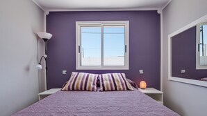 A bedroom with a bed, a window, a bedside lamp, and a wall-mounted mirror.