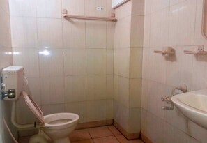 A small bathroom with a toilet, a sink, and a shower area. - Hotel Sapthagiri Nest (Coimbatore)