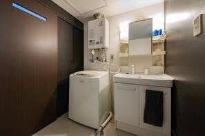 A compact bathroom with a washing machine, a sink, a mirror, and a towel rack. - Blue (Sapporo)