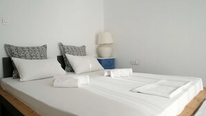 Een opgemaakt bed met witte lakens en meerdere kussens, een bedlampje en een blauwe nachtkastje.