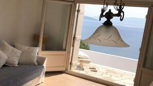 Ein Zimmer mit einem Bett, einer Schlafcouch, einem großen Fenster mit Meerblick und einer Pendelleuchte.