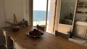 Ein Holztisch mit Obstschale, einer kleinen Dekoration und Blick auf das Meer durch eine offene Tür.