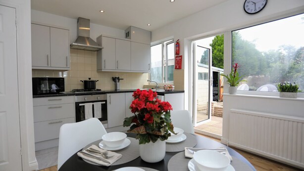 A modern kitchen with white cabinets, a stove, and a dining area with a table set for four.