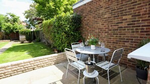A patio area with a round table and chairs, a potted plant, and a brick wall.