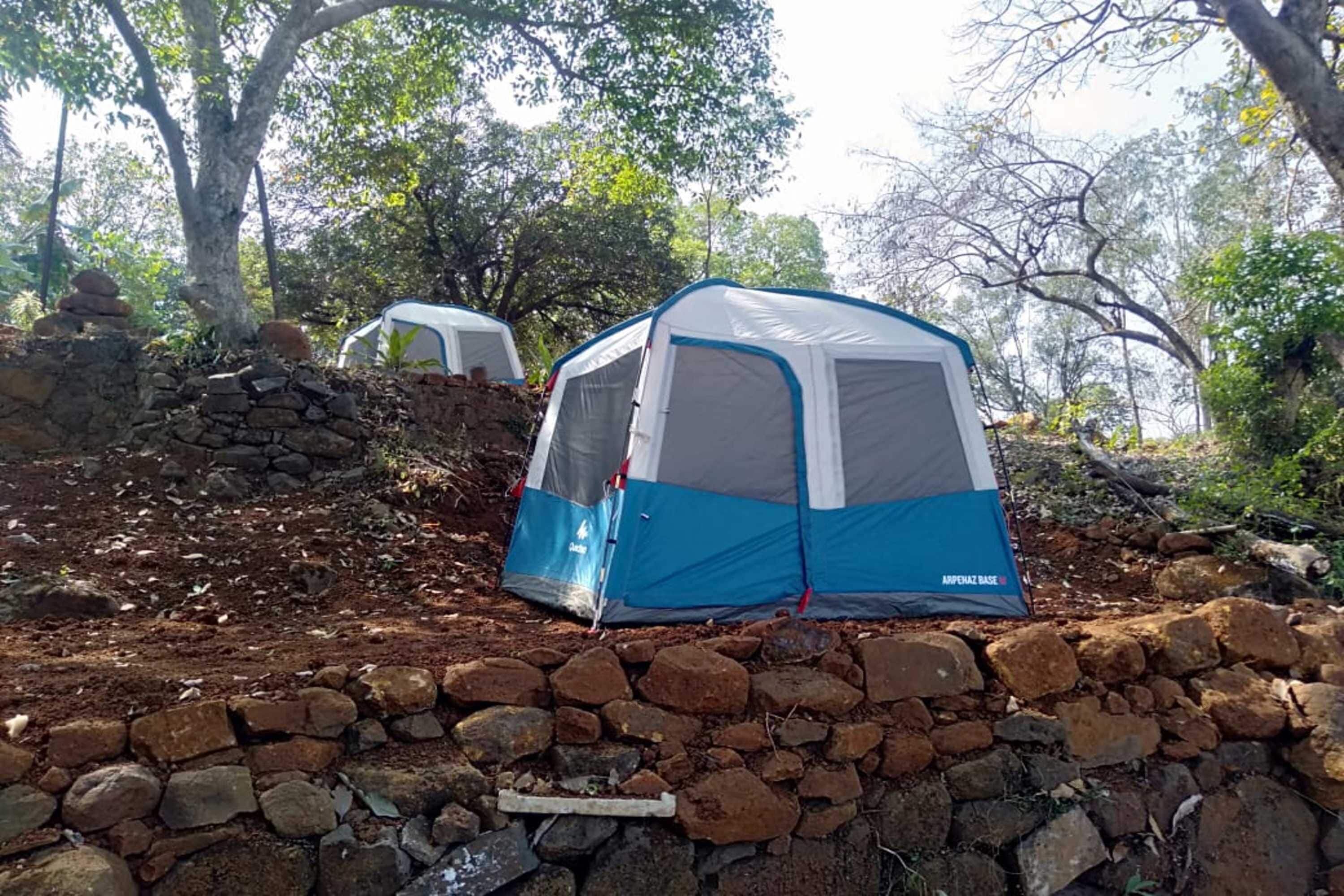 A camping site with two tents set up on a rocky slope surrounded by trees.
