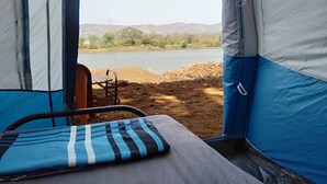 Ein Zelt mit Bett im Inneren, ein Stuhl davor und Blick auf einen See und Hügel.
