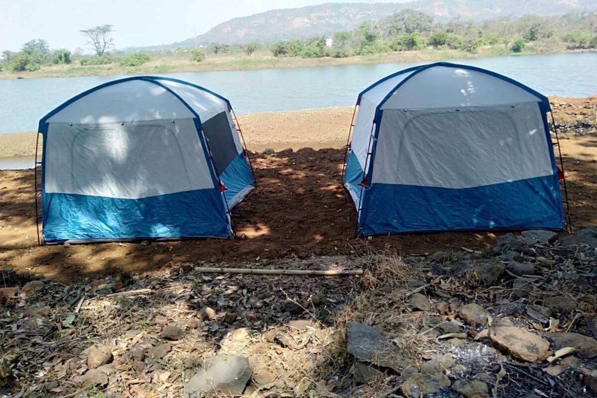Two blue and white tents set up on a sandy beach with a lake and hills in the background.
